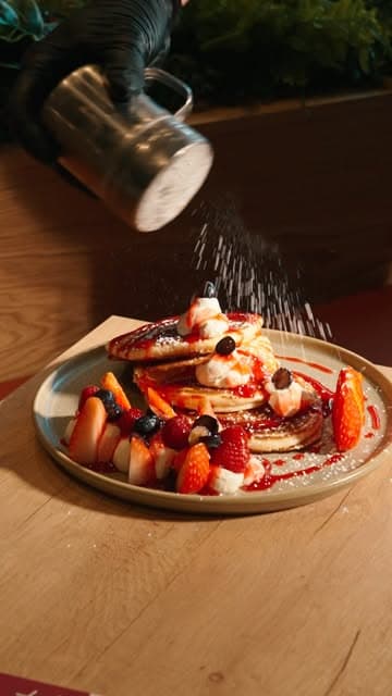 A stack of pancakes with berries and icing sugar